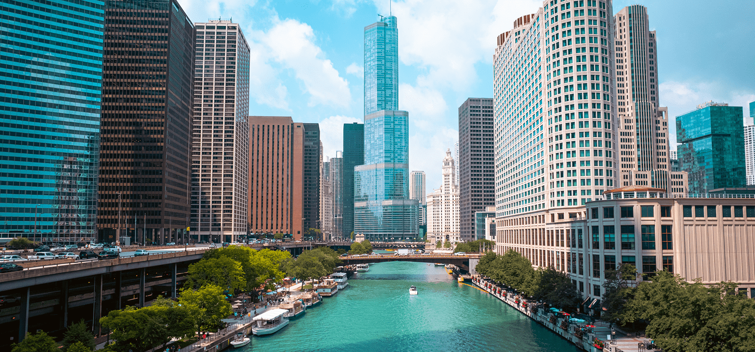 City skyline with river and boats under a blue sky.