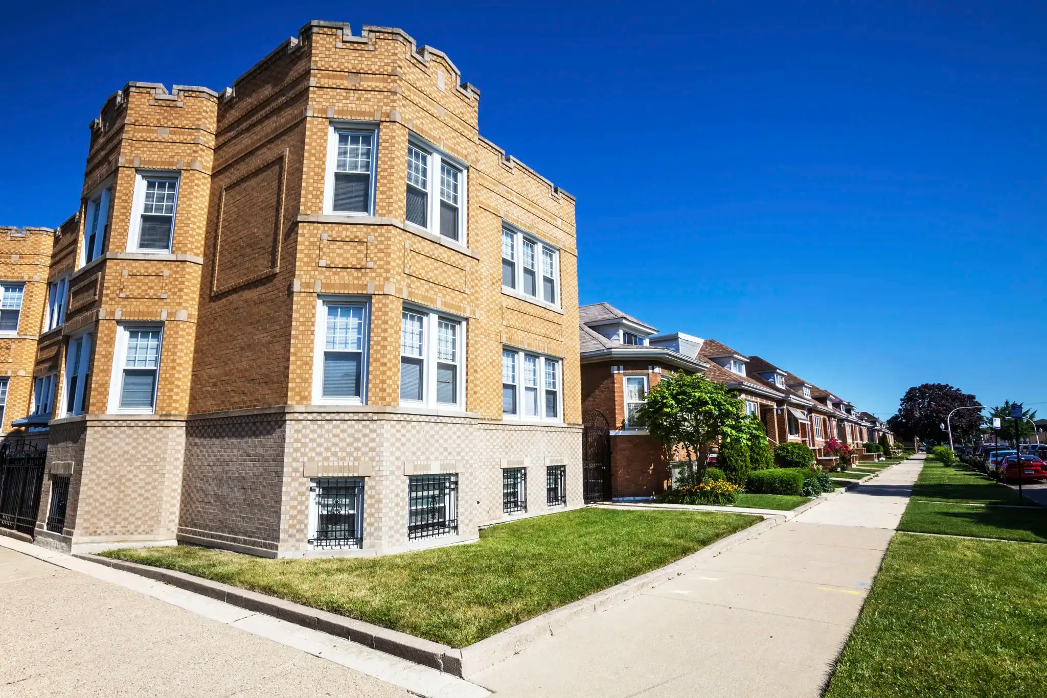 A sunny street with brick apartment buildings and a clear blue sky.