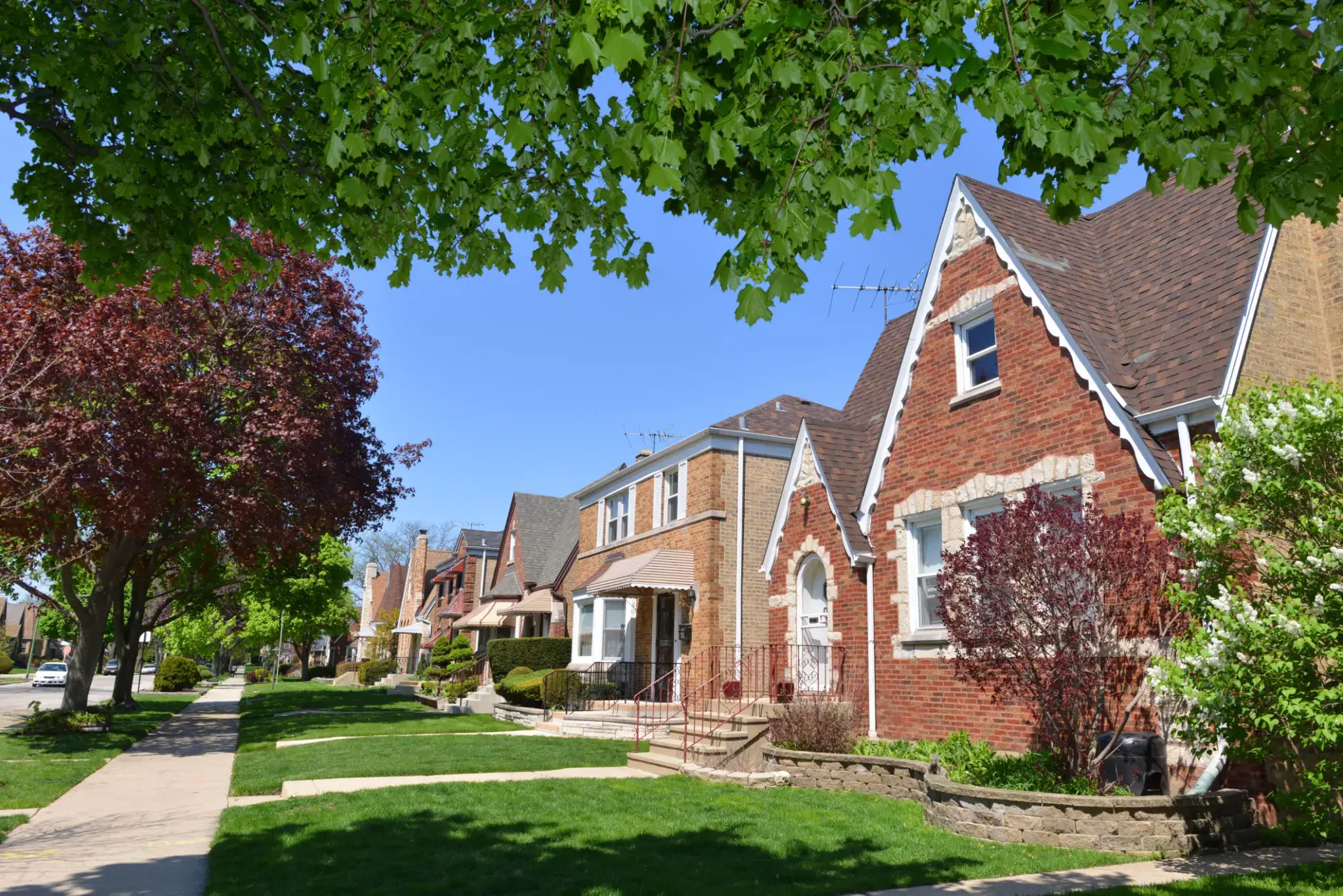 A sunny street with charming brick houses and green trees.