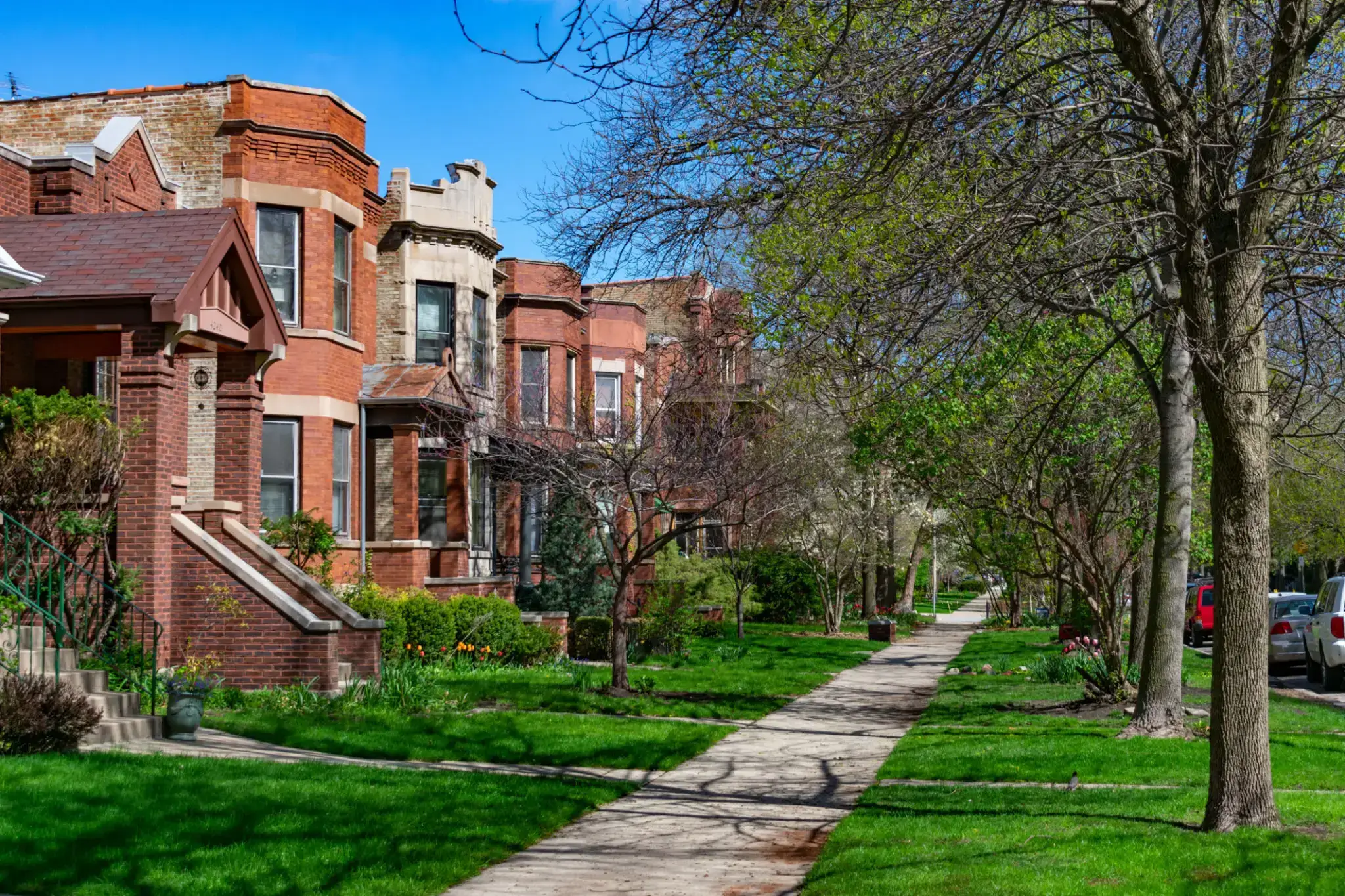 A peaceful residential street with brownstone houses and green lawns.